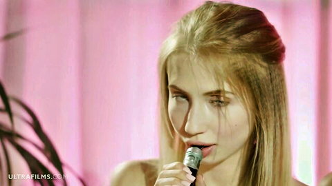 Blonde beauty sensually holding microphone close to lips in pink-lit performance