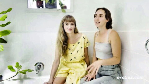 Blonde Laney and cute brunette Olive in yellow dress, smiling in bathroom