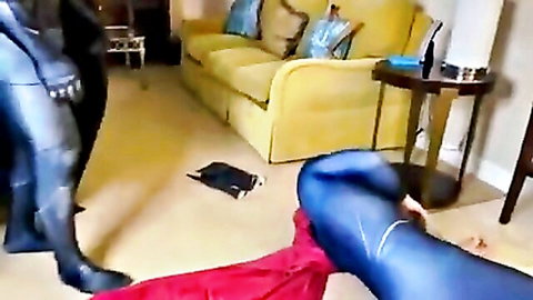Two gay superheroes in shiny blue latex Superman suits groping tight asses near yellow couch