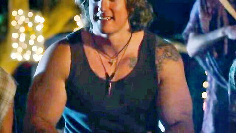 Muscular long-haired man smiling in black tank top at festive outdoor scene