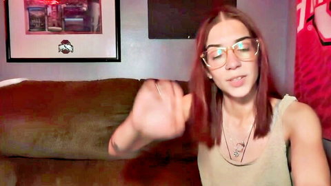 Young redhead teen in glasses gesturing on webcam couch teasing cleavage