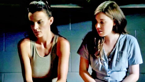 Two skinny brunette girls with fair skin gazing intensely at each other in tank top and button shirt