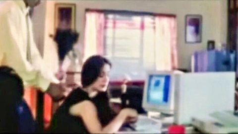 Indian wife at desk in black dress with man behind her