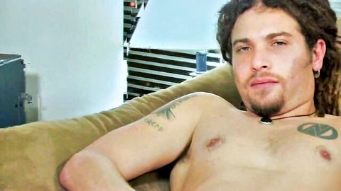 Tattooed dreadlocked guy with piercings lounges shirtless before jerking his pierced cock