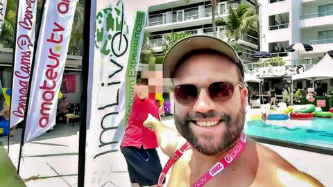 Shirtless smiling man in sunglasses at poolside party with Lamour TV banners