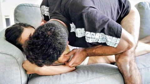 Black stud passionately kissing sexy Arab brunette babe's neck on couch in romantic foreplay