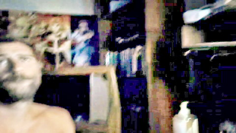 Shirtless bearded man smiling in cluttered webcam room solo tease