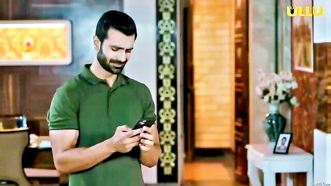 Handsome Indian man in green polo shirt checking phone intently in luxurious room Ullu series