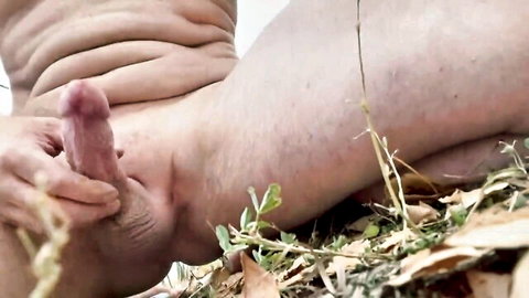 Hairy man strokes thick erect pink cock revealing exposed anus outdoors on grass