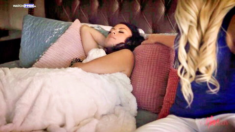 Blonde woman gazes at topless brunette MILF relaxing under fluffy white blanket in bed