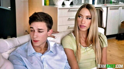 Blonde babe in green top sits close to young guy on couch in kitchen teasing him