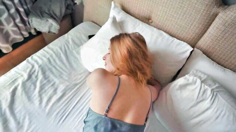 Redhead babe lying seductively on bed in thin gray slip exposing bare back