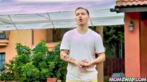 Blonde guy in white t-shirt and yellow shorts gesturing outdoors on momswap patio