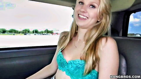 Petite blonde in teal lace bra smiling in bus seat, teasing cleavage