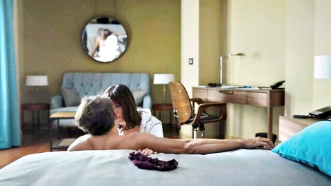 Brunette woman in white blouse passionately kisses naked man's bare back and ass on luxury bed.