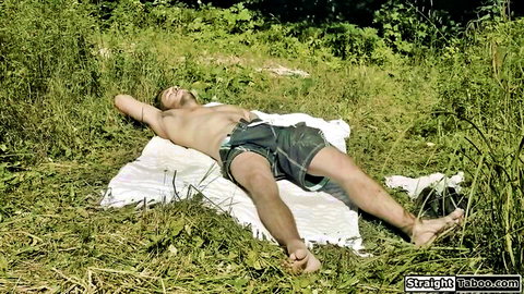 Shirtless athletic man relaxing on blanket in grassy woods, eyes closed