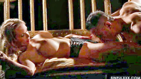 Blonde MILF with big tits lies topless as muscular stud sucks her nipples in bamboo cage.