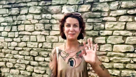 Mathilda 33yo French model smiling and waving in low-cut gold dress with tattoos