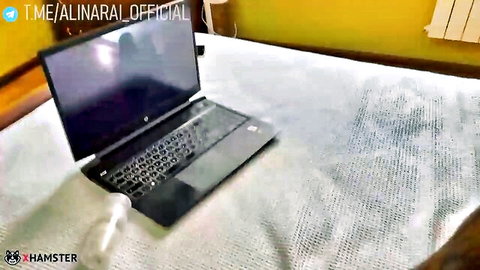 Thick white dildo standing next to black HP laptop on white bedspread