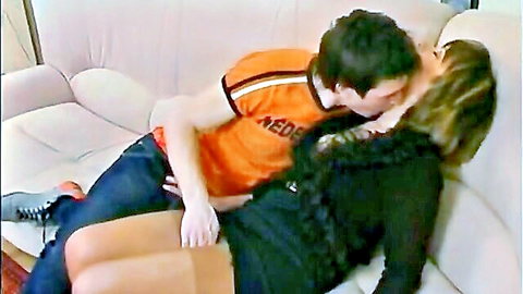 Man in orange shirt passionately kissing blonde woman on couch groping her thigh
