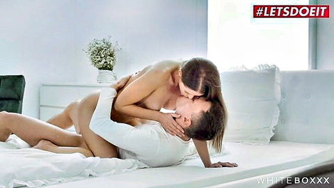 Nude petite woman with small tits straddling and passionately kissing man in white shirt on bed