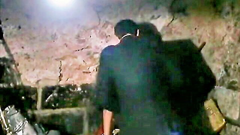 Vintage brunette with ponytail and dark-clad man standing in dimly lit rocky cave