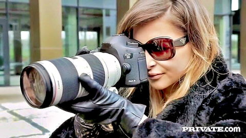 Ria Sunn peering through camera lens in fur coat and sunglasses