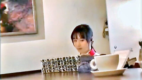 Cute young Japanese girl with pigtails sipping tea at table in red top