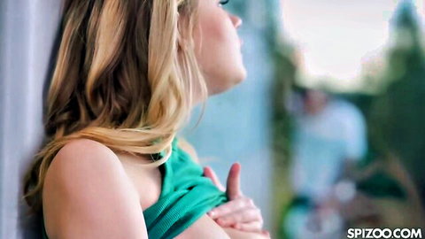 Blonde woman in green tank top, hand on chest, profile view outdoors
