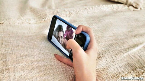 Brunette woman on bed holding phone showing family selfie with child, teasing secretive moans