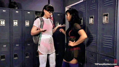 Trans babe in sheer white top and shorts gestures at Asian hottie in mesh top in locker room