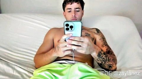 Zaylanez shirtless tattooed hunk in green pants holding phone