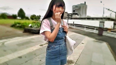 Cute Asian teen in short denim overalls bites nail outdoors