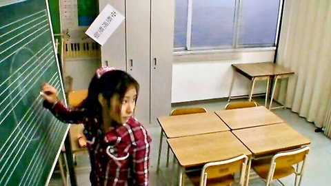 Cute petite Japanese schoolgirl in plaid uniform writing on blackboard