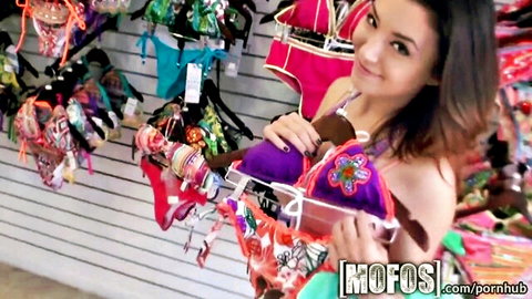 Brunette Latina babe smiling while holding colorful bikinis in store