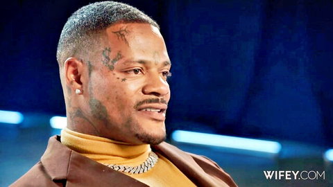 Tattooed black man with face tats smiling in yellow turtleneck and gold chain