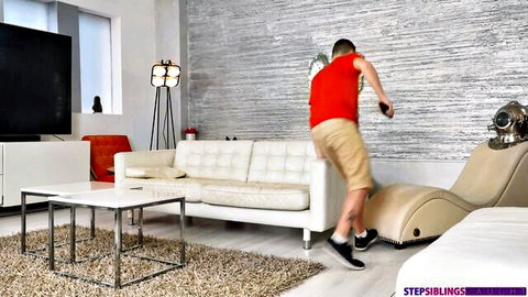 Athletic stepsibling guy in red tank top and shorts jumps with game controller in slave roleplay scene