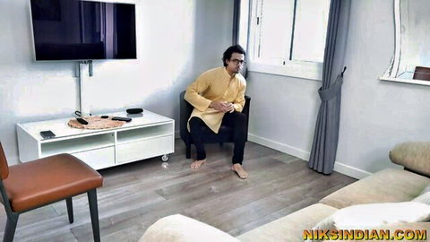 Indian man in yellow kurta squats barefoot on living room floor teasing viewers