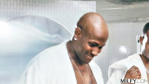 Two muscular black BBC studs in open white robes smiling teasingly in gym locker room