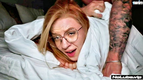 Redhead teen with glasses moans as tattooed guy chokes her neck under sheets on bed