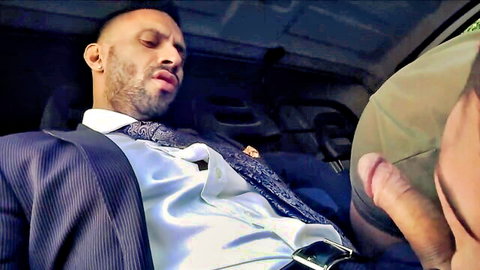 Bearded suited man receives oral from darker-skinned partner in car