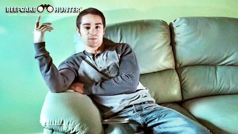 Latino beefcake Jesse lounging casually on couch in hoodie and jeans