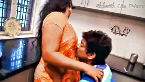 Busty Indian MILF in saree passionately kissing young man in kitchen embrace