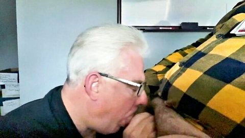 Elderly man with glasses performing oral sex on larger man's crotch