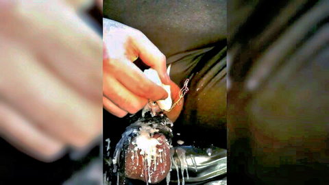 Tattooed hand drips hot wax from candle onto man's exposed balls and cock base in BDSM CBT wax play