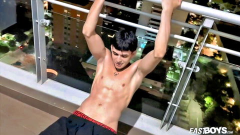 Muscular young gay stud hangs shirtless from balcony railing in tight red underwear teasing bulge
