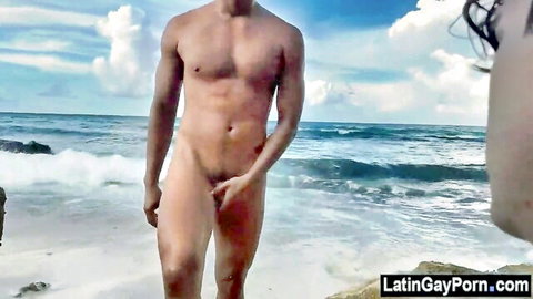 Muscular Latin man nude on sunny beach, hand on cock, outdoor gay adventure