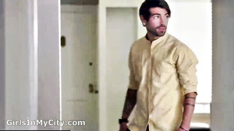 Tattooed man in light shirt stands in doorway, intense gaze