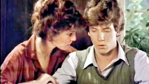 Brunette woman with curly hair intimately close to shaggy haired man in vintage scene