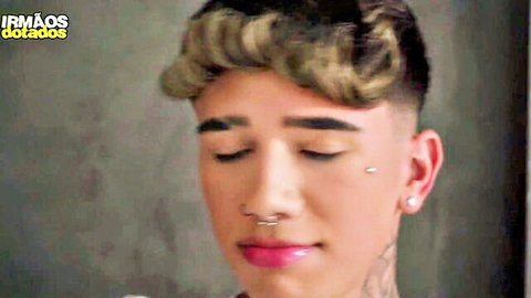 Closeup of tattooed twink with piercings, makeup and curly hair looking seductive